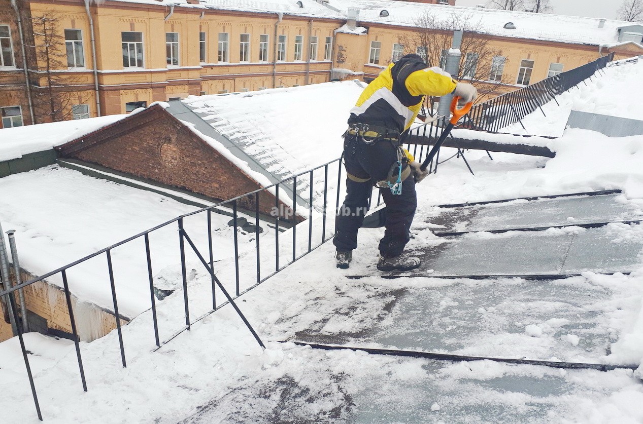 Промышленный альпинист счищает снег прямо у края крыши