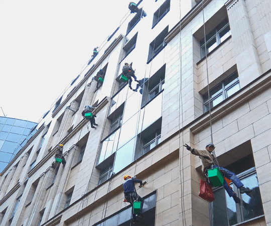 группа промышленных альпинистов чистит фасад здания