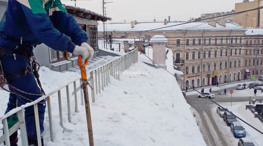 Промальпинист счищает снег с крыши, стоя за бортиком