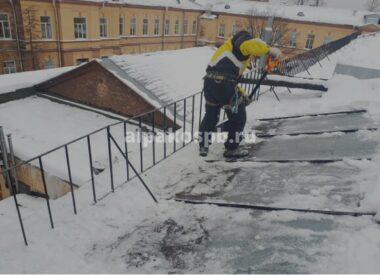 Промышленный альпинист у края крыши счищает снег