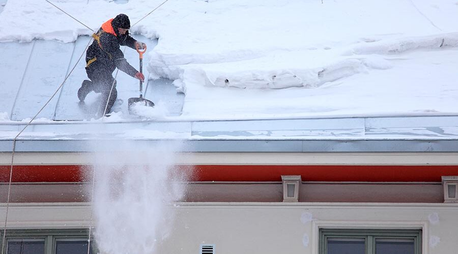 Промальпинист со страховкой снимает обледенение и снег с крыши